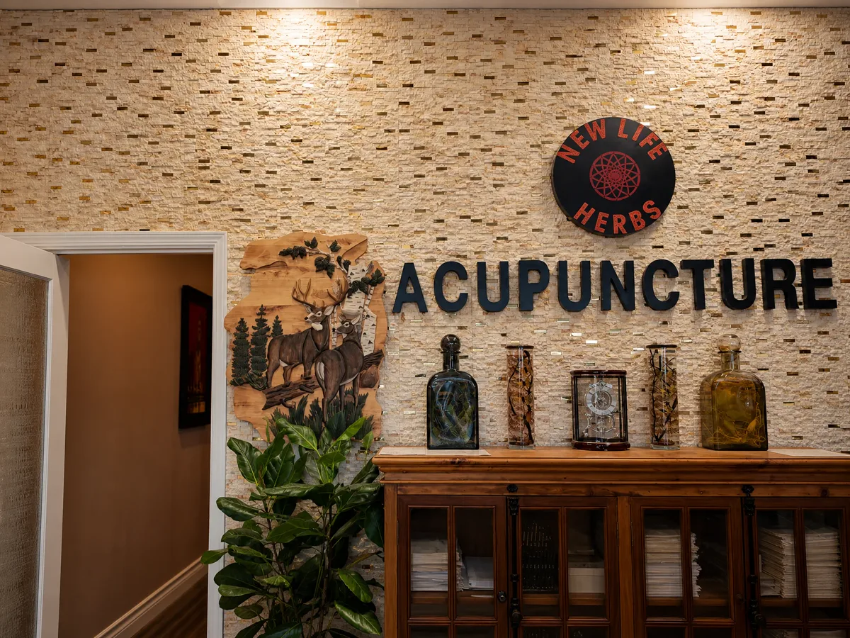 Reception wall with the round New Life Herbs logo, the word Acupuncture, a carved deer panel and herbal tincture bottles