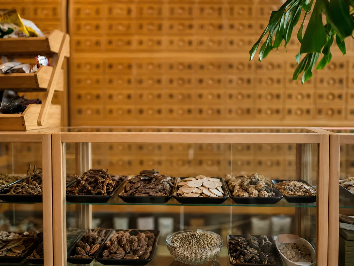 Glass display cases of dried Chinese herbs in front of a wall of wooden herb drawers